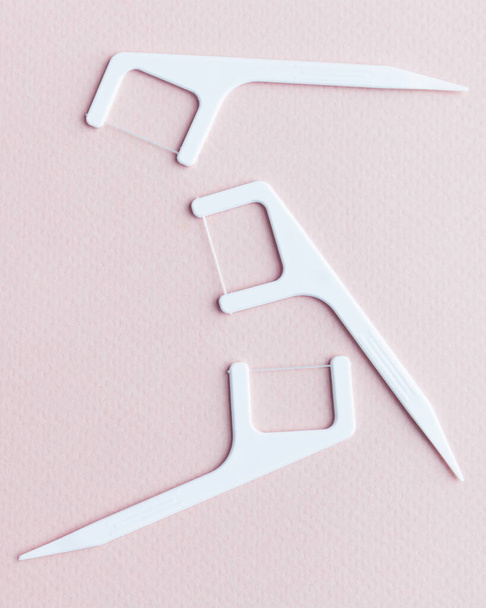 Vista superior del mondadientes de plástico desechable con hilo dental para un cuidado interdental eficaz aislado sobre fondo rosa claro. Higiene oral.  - Foto, Imagen