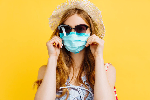 Young happy woman in medical protective mask and summer hat, in summer clothes, on isolated yellow background - Foto, imagen