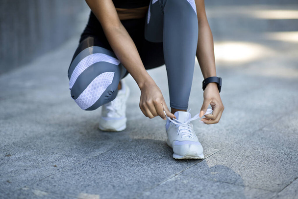 Primo piano della ragazza nera in abbigliamento sportivo lacci delle scarpe prima di fare jogging - Foto, immagini