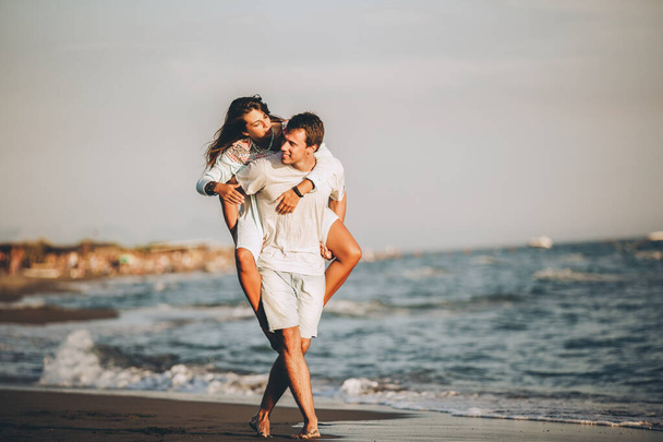 Πορτρέτο του άντρα που κουβαλάει την κοπέλα του στην πλάτη του στην παραλία - Φωτογραφία, εικόνα