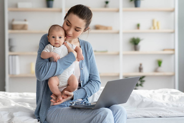 Portré a fiatal boldog anya gazdaság újszülött baba és használata laptop számítógép - Fotó, kép