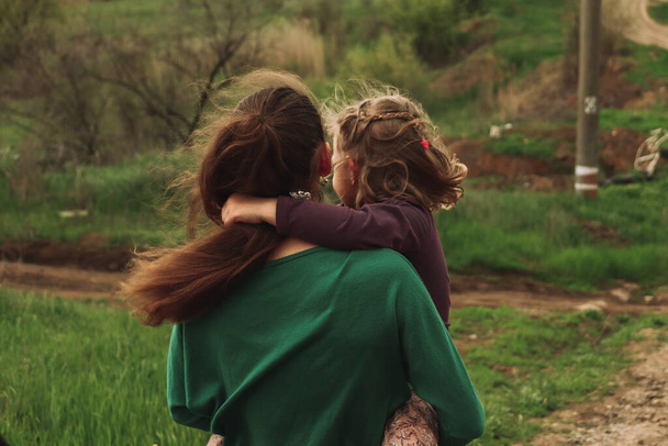 Κόρη και μαμά. Αδερφές στη φύση. Η μητέρα κρατά το ξανθό παιδί στην αγκαλιά της.. - Φωτογραφία, εικόνα