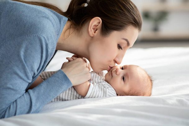 Материнская любовь. Молодая красивая женщина целует своего очаровательного новорожденного сына дома - Фото, изображение