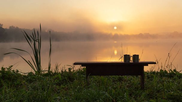 Bench és két csésze forró kávé a háttérben a felkelő nap. Nyári szabadság koncepciója - Fotó, kép