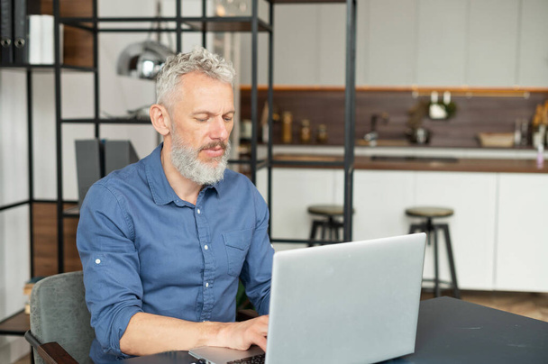 Focused mature man typing on the keyboard, senior male using laptop for remote work - 写真・画像
