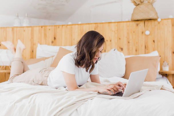Woman Relaxing On Bed Using Laptop Computer For Video Call in modern flat - Zdjęcie, obraz