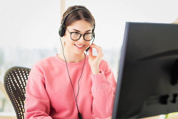 Customer service assistant wearing headset while sitting behind her computer and working from home. Home office.  - 写真・画像