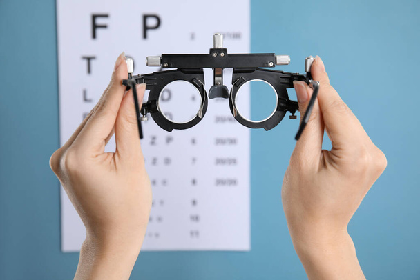 Woman holding trial frame against eye chart test on blue background, closeup. Ophthalmologist tool - Foto, immagini