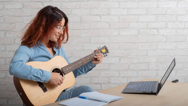 A woman is learning to play the guitar online. Remote music lesson - Фото, изображение