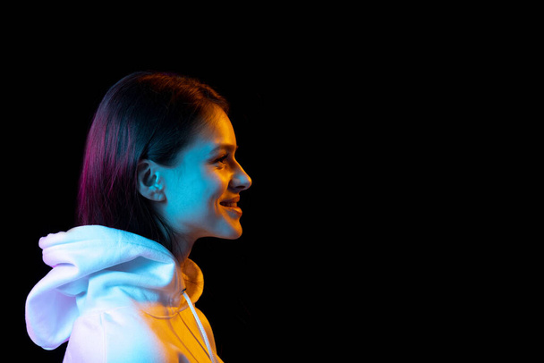 Side view of young beautiful girl isolated over dark background in neon light. - Fotografie, Obrázek