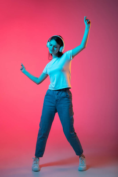 Full-length portrait of young beautiful girl isolated on pink background in neon - 写真・画像