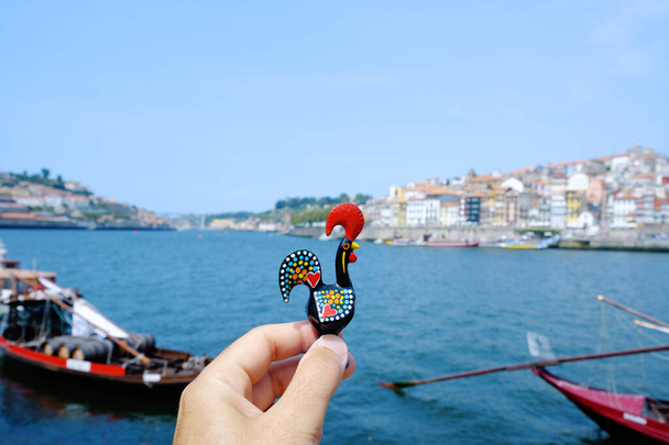 gros plan d'un jeune caucasien tenant un coq traditionnel de Barcelos, emblème du Portugal, à Porto, sur la rivière Douro avec le quartier de Ribeira à droite - Photo, image