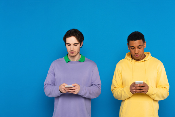 διαφυλετικοί φίλοι κοιτάζοντας smartphones απομονωμένα σε μπλε - Φωτογραφία, εικόνα