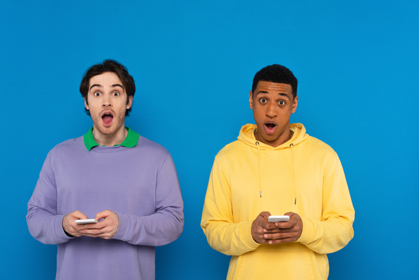 amigos interracial con teléfonos inteligentes en manos aisladas en azul - Foto, imagen