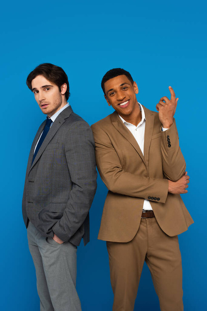 Elegant interracial men in suits standing confidently isolated on blue - Zdjęcie, obraz