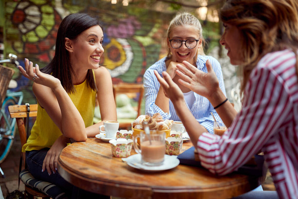 A group of female students is enjoying a friendly talk while having a drink in a bar garden on a beautiful day. Leisure, bar, friendship, outdoor - Fotografie, Obrázek