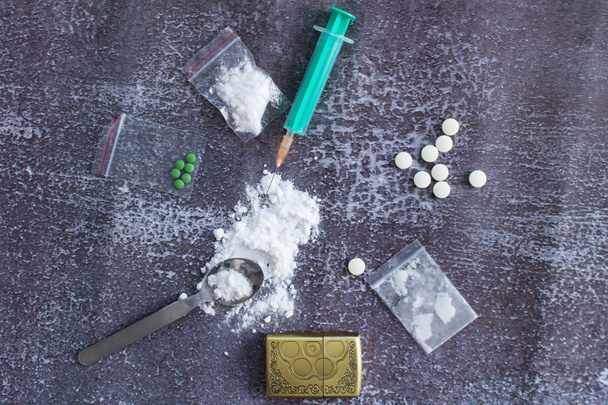 Aids, Pillen und Medikamente für Drogenkonsumenten. Amphetamintabletten, Methamphetamin in einem Beutel, möglicherweise Kokain oder Heroin, und eine Spritze mit Nadel, Löffel und Feuerzeug. - Foto, Bild