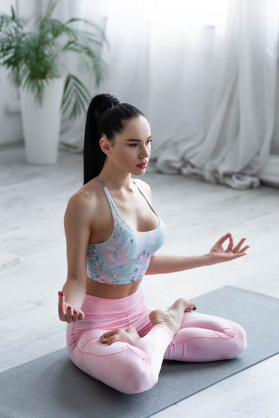 young brunette woman meditating in lotus pose at home - Foto, imagen