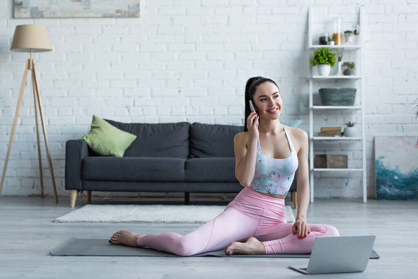 glückliche junge Frau telefoniert auf Yogamatte neben Laptop - Foto, Bild