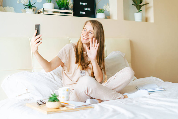 Νεαρή γυναίκα που παίρνει μια selfie στο smartphone, ενώ κάθεται στο κρεβάτι - Φωτογραφία, εικόνα