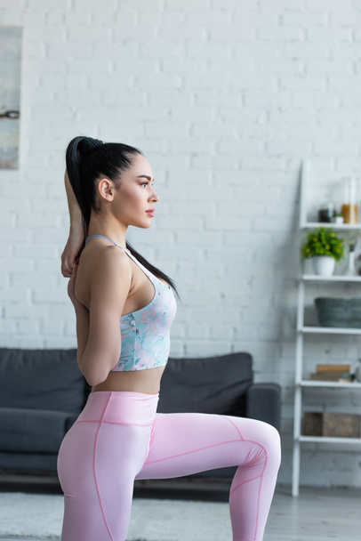 vista lateral de la mujer bonita haciendo ejercicio de estiramiento con las manos detrás de la espalda - Foto, Imagen