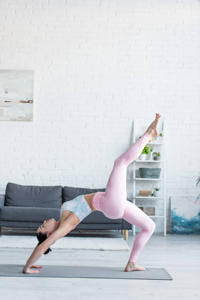 side view of young woman in sportswear practicing yoga in one legged wheel pose - Фото, зображення