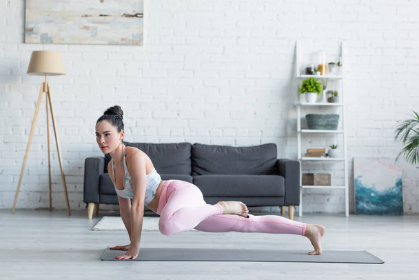 young woman in sportswear practicing in one legged plank pose at home - Foto, Bild