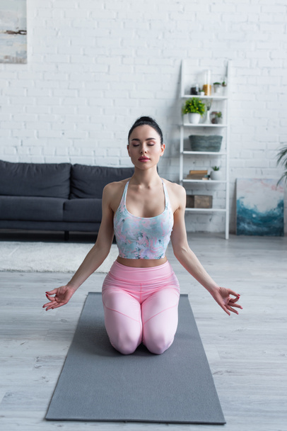 junge Frau in Sportkleidung meditiert in Heldenpose auf Yogamatte - Foto, Bild