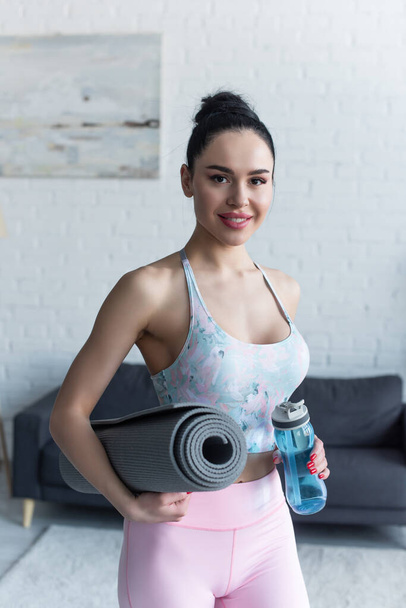happy woman with sports bottle and fitness mat smiling at camera - 写真・画像