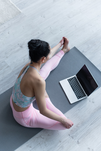 overhead view of brunette woman practicing yoga near laptop with blank screen - Foto, Imagen