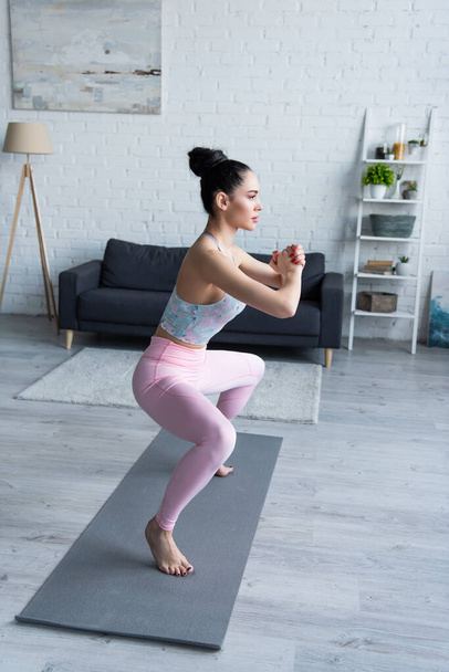 hübsche Frau in Stuhlpose mit geballten Händen, während sie zu Hause Yoga praktiziert - Foto, Bild