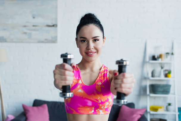 cheerful woman smiling at camera while exercising with dumbbells - 写真・画像