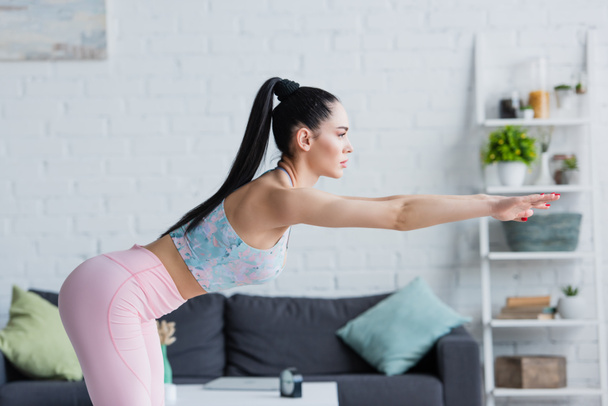 side view of brunette woman in sportswear doing forward bend exercise with outstretched hands - Photo, Image