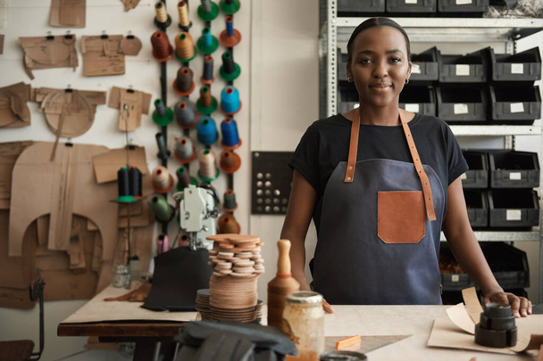 Portrait of a young African female leather worker standing at a workbench in her artisanal leather studio - Valokuva, kuva