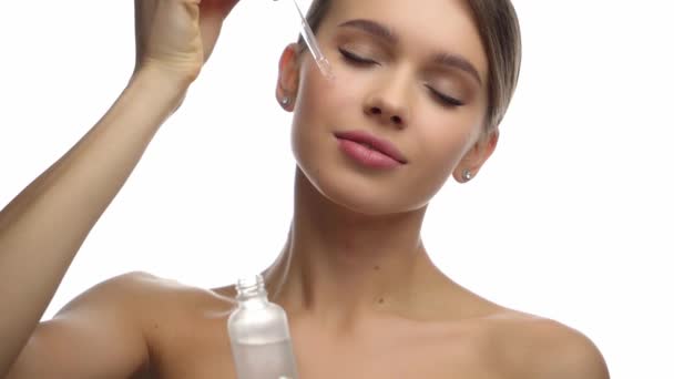 cámara lenta de la mujer joven aplicando suero hidratante aislado en blanco - Metraje, vídeo
