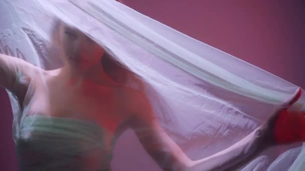 young woman looking at camera through chiffon drapery on purple  - Záběry, video
