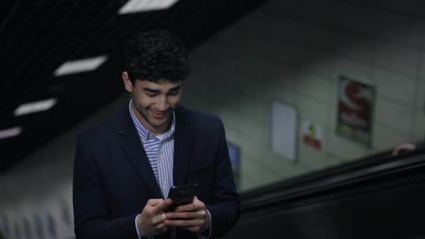 Positive businessman using smartphone on escalator - Кадри, відео