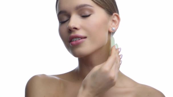 νεαρή γυναίκα μασάζ στο λαιμό με ξύστρα πέτρας νεφρίτη απομονώνονται σε λευκό  - Πλάνα, βίντεο