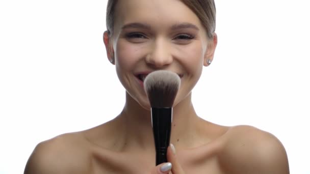 boldog fiatal nő gazdaság kozmetikai kefe és alkalmazása por elszigetelt fehér  - Felvétel, videó
