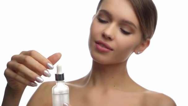mujer joven sosteniendo botella y pipeta con suero aislado en blanco - Imágenes, Vídeo