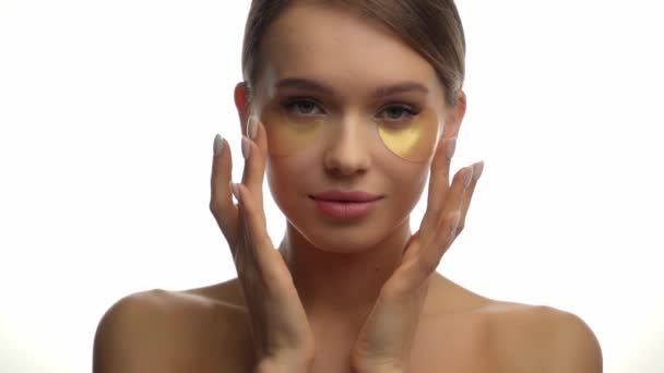 mujer joven aplicando parches de ojos dorados sobre blanco  - Metraje, vídeo
