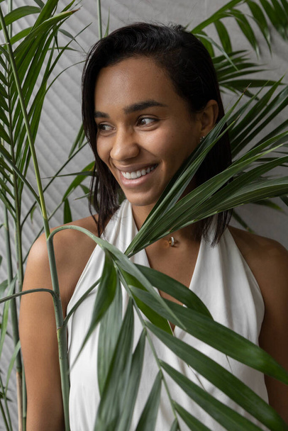 face of a cheerful and beautiful brunette woman who is smiling, around there are leaves of a plant, she has short hair and a white blouse, studio - Фото, изображение