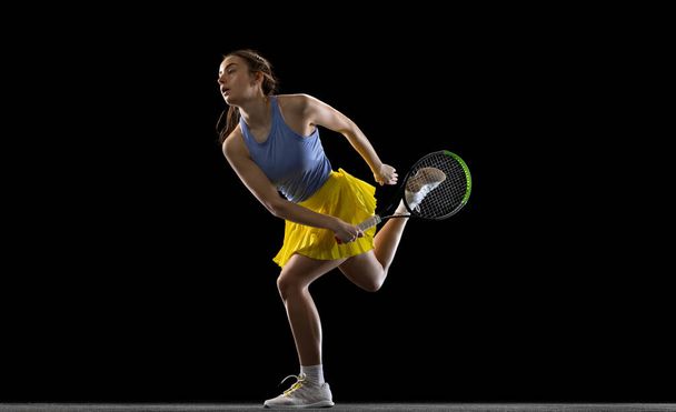 Young caucasian woman playing tennis isolated on black studio background in action and motion, sport concept - Foto, Imagen