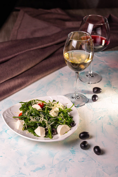 Salad with mozzarella and arugula in a white plate with wine - Foto, Bild
