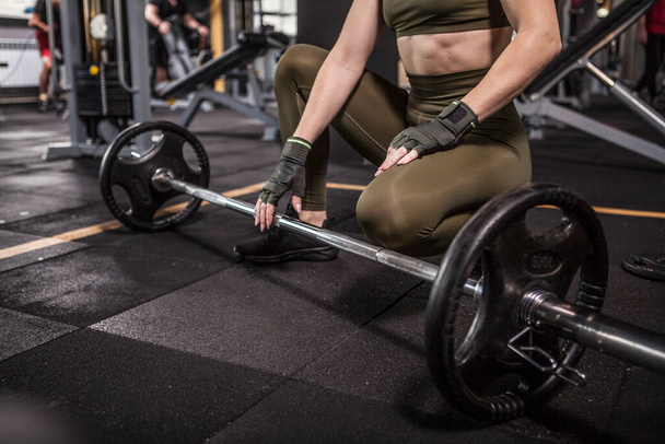 Unrecognizable sportswoman with fit body resting during barbell workout at gym - Photo, Image