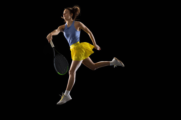 Young caucasian woman playing tennis isolated on black studio background in action and motion, sport concept - Фото, изображение