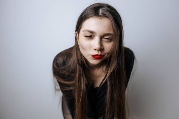 A beautiful girl with red lips winks. Large portrait on a light background - Photo, Image