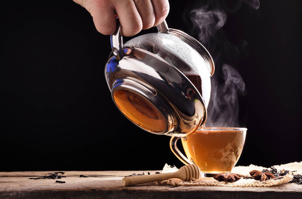 Proceso de ceremonia del té Ceremonia del té Una taza de té negro recién hecho se coloca en una mesa de madera donde una cálida luz suave brilla sobre un fondo negro oscuro. - Foto, imagen