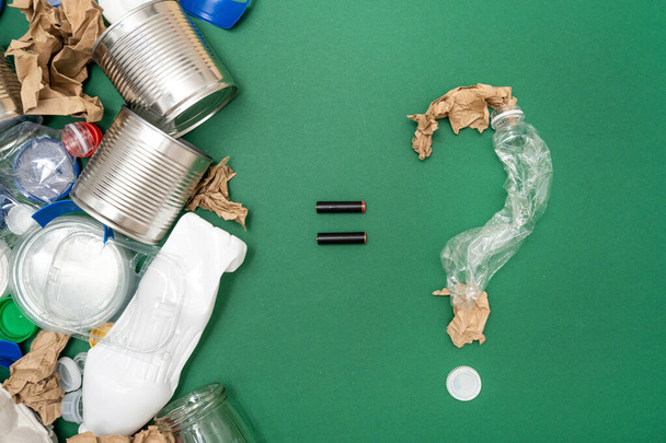 Different types of garbage paper, plastic, metal and other assorted waste in composition with question mark made of trash isolated on green background. Recycling and ecology pollution concept - Photo, Image