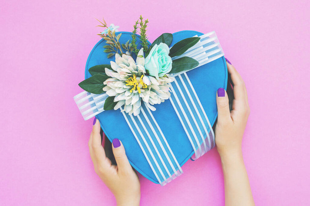 La mano de la mujer sostiene una caja de regalo azul corazón aislado en rosa. - Foto, imagen